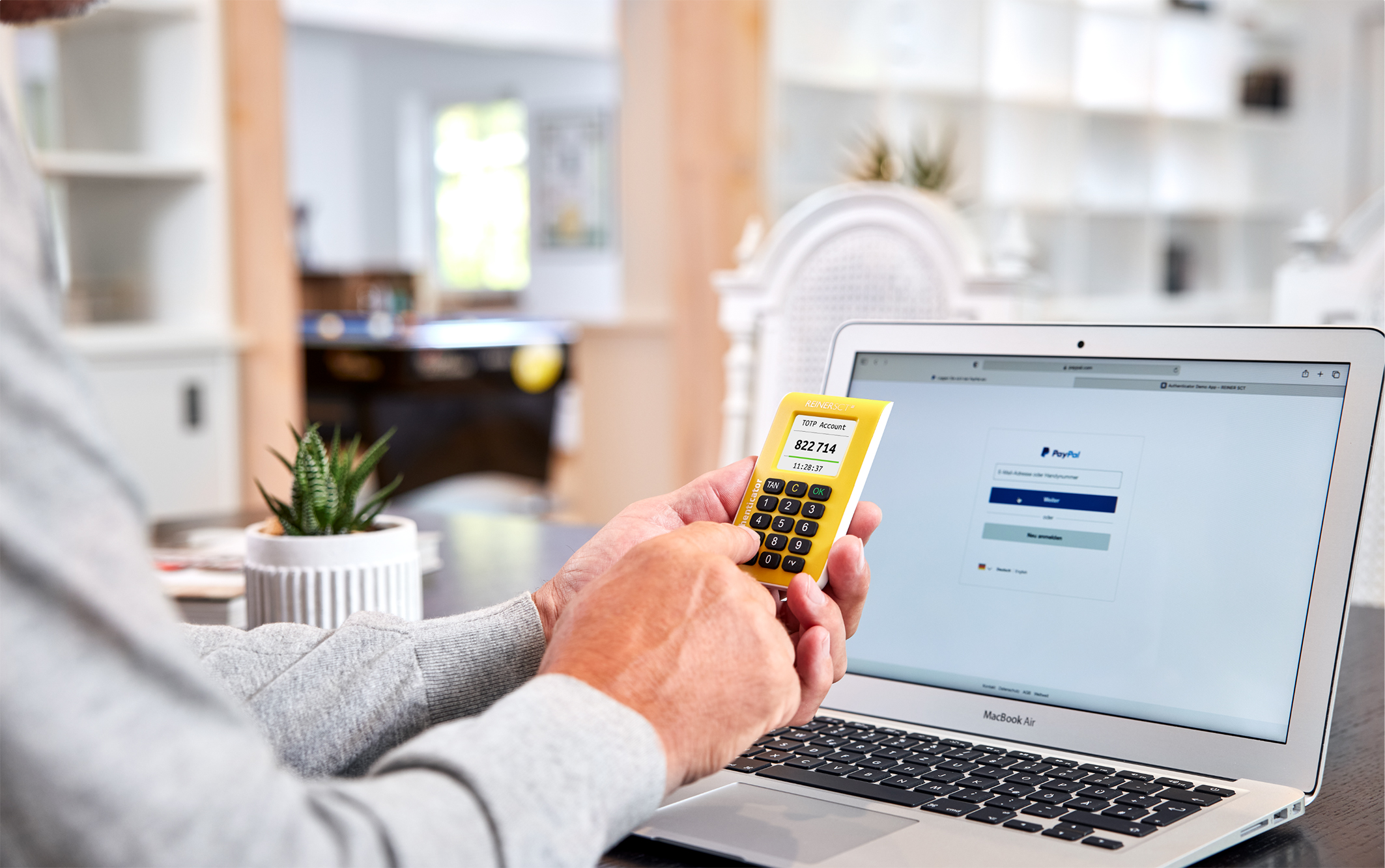 Reiner SCT Authenticator in einer Hand vor einem Rechner Reiner SCT Authenticator in einer Hand vor einem Rechner